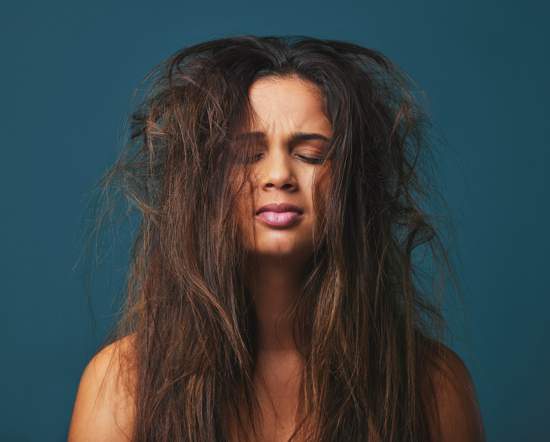 Studio shot of a beautiful young woman with messy hair posing against a blue background